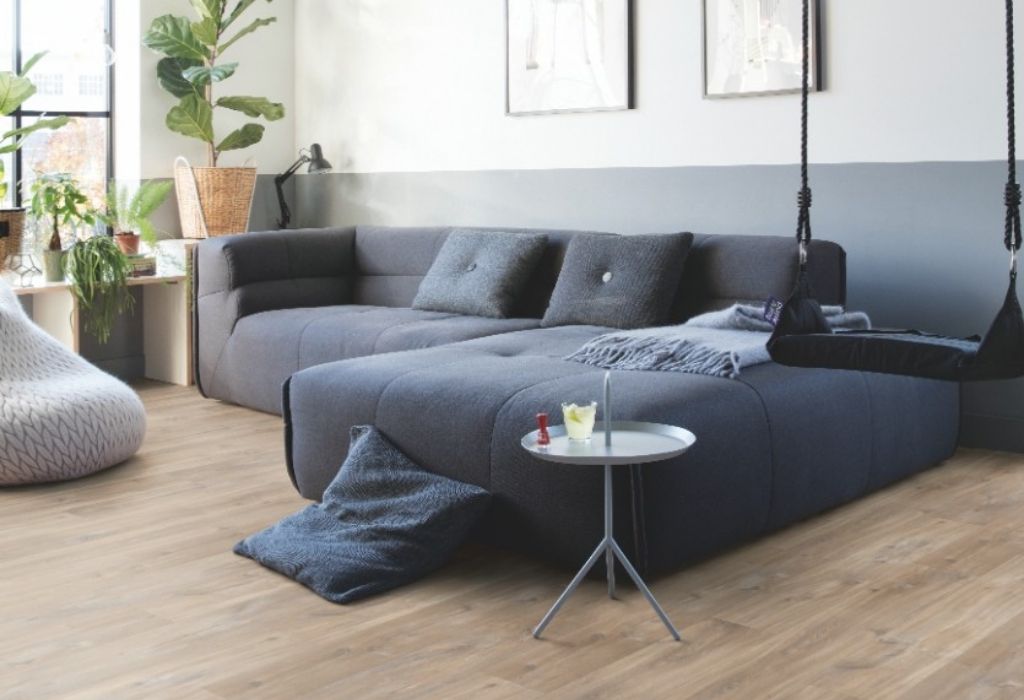 Salon z drewnianą podłogą i dużą, szarą sofą
